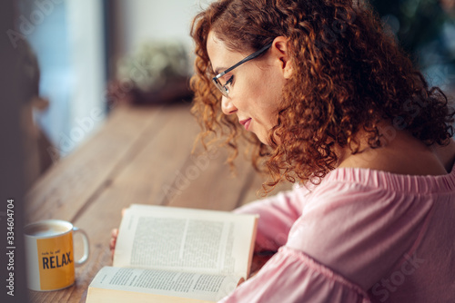 Fotomural Young red hair woman with eyeglasses is sitting and reading a book