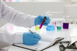 © H_Ko - Employee of the chemical laboratory teacher chemist holds a silvery pen in his hand makes notes in the diary records test data from reactions examining test tubes with the substance arm in gloves.