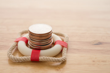 Wall Mural - Stacked coins in red lifebuoy or lifebelt with wooden background copy space. Assets wealth, money saving or money investment protection and security by insurance concept. Risk management analysis.