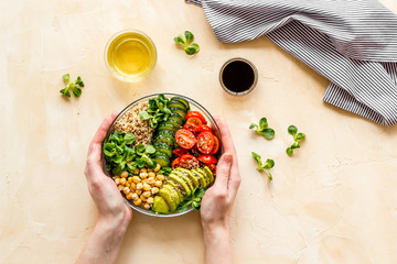 Wall Mural - Quinoa, avocado and chickpeas in bowl in hands - balanced healthy food - on beige table. Top view