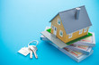House model, bill dollar banknotes and key on blue background. Money saving for new house, home loan, reverse mortgage and real estate property business concept