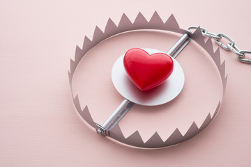 Red heart in a trap on pink background. Online internet romance scam concept. Love is bait or victim.