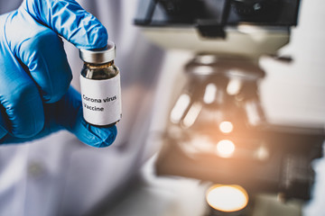 doctor wearing protective gloves holding COVID-19 vaccination vaccine cure for ill patients, using microscope researching corona virus microscopic cells testing vaccination cure, in medical laboratory