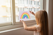 © Алина Бузунова - Kid painting rainbow during Covid-19 quarantine at home. Girl near window. Stay at home Social media campaign for coronavirus prevention, let's all be well, hope during coronavirus pandemic concept