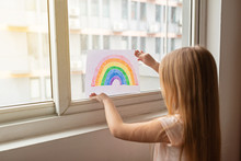 Kid Painting Rainbow During Covid-19 Quarantine At Home. Girl Near Window. Stay At Home Social Media Campaign For Coronavirus Prevention, Let's All Be Well, Hope During Coronavirus Pandemic Concept