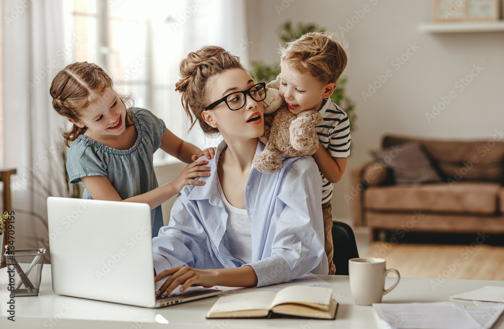 Little children distracting dedicated young woman working on laptop at home. - obrazy, fototapety, plakaty 