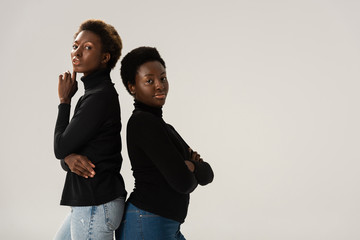 Wall Mural - confident african american girls in black turtlenecks standing back to back isolated on grey