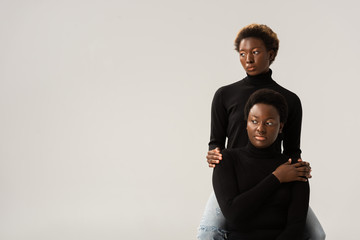 Wall Mural - african american friends in black turtlenecks hugging isolated on grey