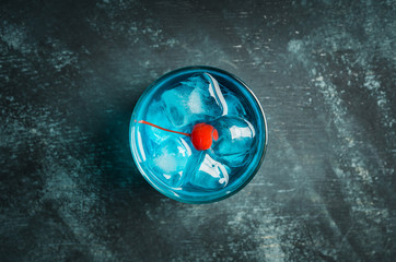 Blue old fashioned cocktail with cherry on the rustic background. Selective focus. Shallow depth of field.