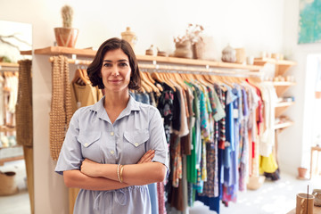 Sticker - Portrait Of Smiling Female Owner Of Fashion Store Standing In Front Of Clothing On Rails