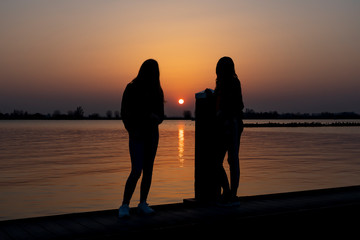 Two young women relaxing during  sunset on a landing stage at the Lake Zoetermeerse Plas in Zoetermeer, The Netherlands 2