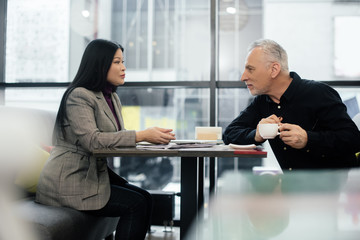 Wall Mural - side view of businessman and asian businesswoman talking in cafe