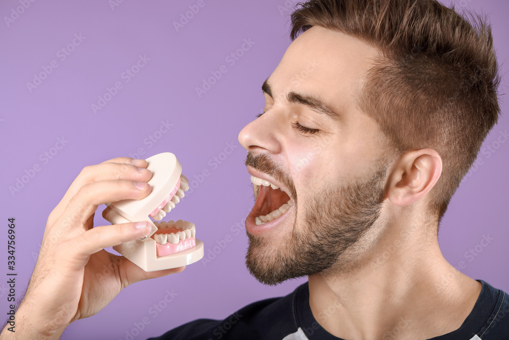 Happy young man with plastic jaw model on color background
