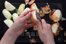 Top View Of Woman Hands Peeling Off With Knife Cutted In Half Unpeeled Onion On The Black Background