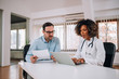 © bnenin - Female doctor, resident, using a laptop while sitting at desk with mentor who looking and holding paper document.