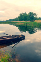 Wall Mural - Wooden boat with oars on the river bank with reflection of clouds in summer