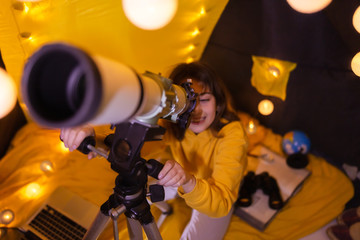 Wall Mural - small girl using telescope at home living room in a tent.