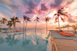 Beautiful sunset at a beach in tropics. Summer landscape vacation or travel landscape under amazing colorful sky. Luxury lifestyle with infinity swimming pool, beach resort hotel, palms sun beds