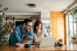 © bnenin - Portrait of a smiling couple looking at laptop together at cozy home office.