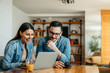 © bnenin - Portrait of smiling man and woman in denim shirt sitting at wooden desk and looking at laptop.