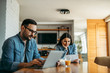© bnenin - Couple sitting at kitchen table, reading letter and using laptop.