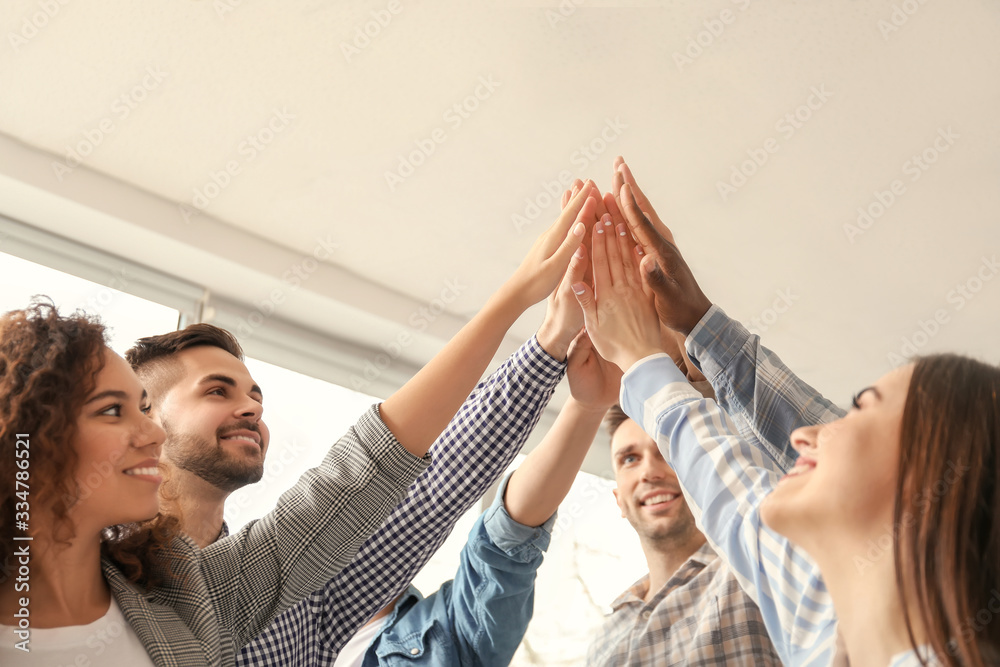 Group of people putting hands together indoors. Unity concept