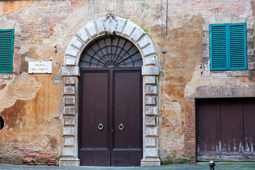 Poster - old massive iron doors in a medieval house with dilapidated plaster on the wall, Piazza del Conte, Siena, Italy