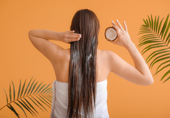 Beautiful young woman applying coconut oil on her hair against color background