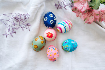 Happy easter Flat lay with Easter eggs painted in different colors on a white fabric with flowers for easter holiday celebration.