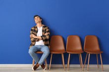 Waiting Young Man Sitting On Chair Near Color Wall