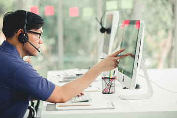 Wall Mural - Young handsome male customer support phone operator with headset working in call center. Handsome male call center worker talking with a client and using computer in office