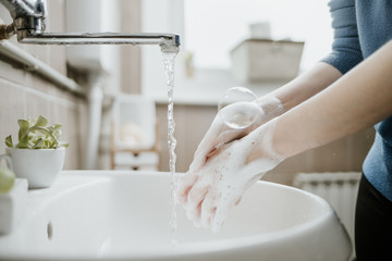 Closeup of a woman washing her hands in bathroom to prevent Covid-19 viral infection. Recommended washing with soap and running water during coronavirus pandemic.