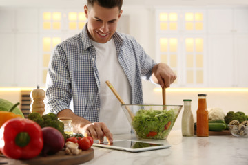 Canvas Print - Man with tablet cooking salad at table in kitchen