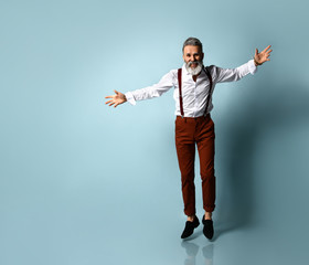 Wall Mural - Aged man in white shirt, brown pants and suspenders, black loafers. He spread his hands and running to you, blue studio background