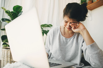 Young woman worries about losing job, depression. Unemployment and economic crisis. Financial instability. Sad girl crying from bad news, sitting with laptop home alone during quarantine.