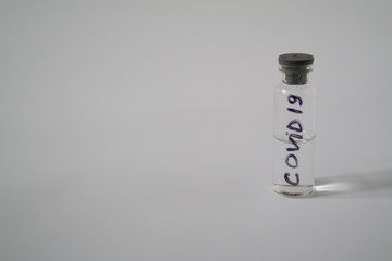 Medical test tube with a transparent liquid with inscription COVID-19 on a gray background. An isolated flask containing an analysis virus or vaccine. The concept of a drug.