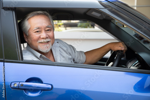Asian senior man driving a car and smile happily with glad positive expression during the drive to travel journey, People enjoy laughing transport and drive thru concept