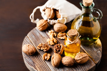 Concept of vegetable fat and oils for cooking and cosmetology. Glass bottle with essence, raw walnut peeled and in their shells. Wooden board, dark wooden background, close up, macro