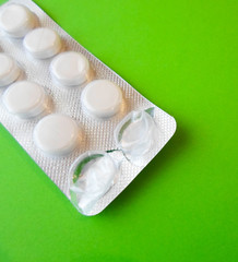 white pills on a green background. snow-white round antibiotics against viruses