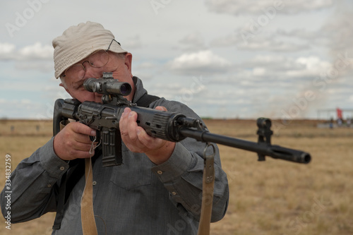 elderly man, war veteran, chooses sniper rifle with telescopic sight in gun shop. Pensioner wants to protect your home. concept of weapons for self-defense