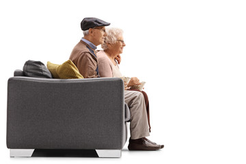 Poster - Profile shot of a senior man and woman sitting on a sofa and eating popcorn