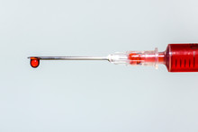 Hypodermic Needle Dripping Red Fluid Over A Pale Out Of Focus Background