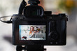 © artiemedvedev - Display of camera recording video blog for blonde beauty blogger woman with make-up at home studio. Influencer vlogger girl live streaming cosmetics masterclass. Online learning and marketing concept.