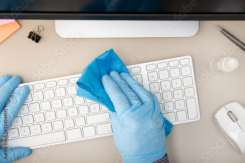 Fotografía Hand with protective glove cleaning a keyboard with disinfectant