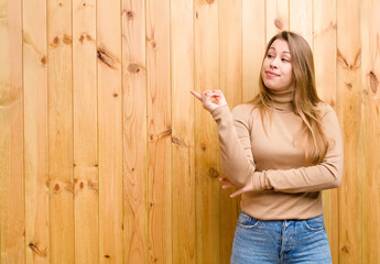 young blonde woman smiling happily and looking sideways, wondering, thinking or having an idea