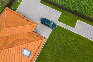 Wall Mural - Aerial top view of house shingle roof with attic windows and black car on paved yard with green grass lawn.