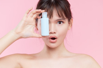 Beauty Woman Face. Close up of young asian woman with fresh skin holding a bottle of cream in hand. girl Applying a Cream Bottle Template cosmetic product under the eyes. Mockup. Skin care concept.