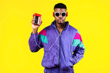 Fototapeta Boho - African American young man, in a jacket in the style of the 90s, with a retro cassette player, hears music, the mood of dancing and fun, yellow and purple colors