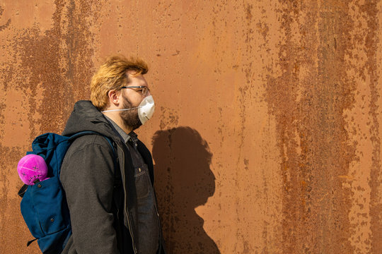 hipster man in medicine mask portrait with bag and pink doll shadow on rusty wall background empty copy space for your text here, urban pollution style photography quarantine and self protection