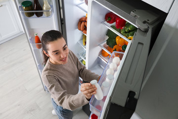 Poster - Young woman taking yoghurt out of refrigerator indoors, above view